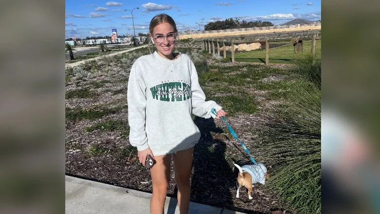 A teenage girl smiles while walking a dog outdoors.