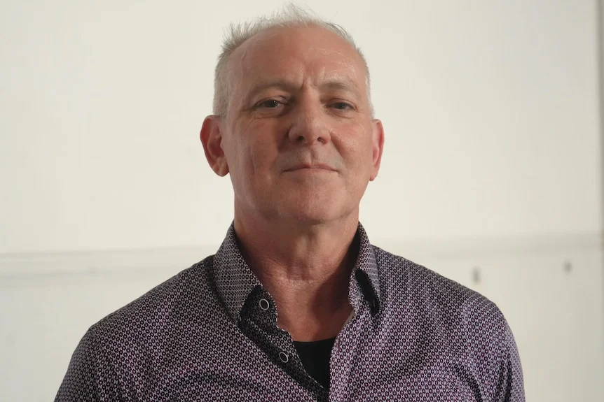 A close-up of a man looking at the camera with a neutral expression. 