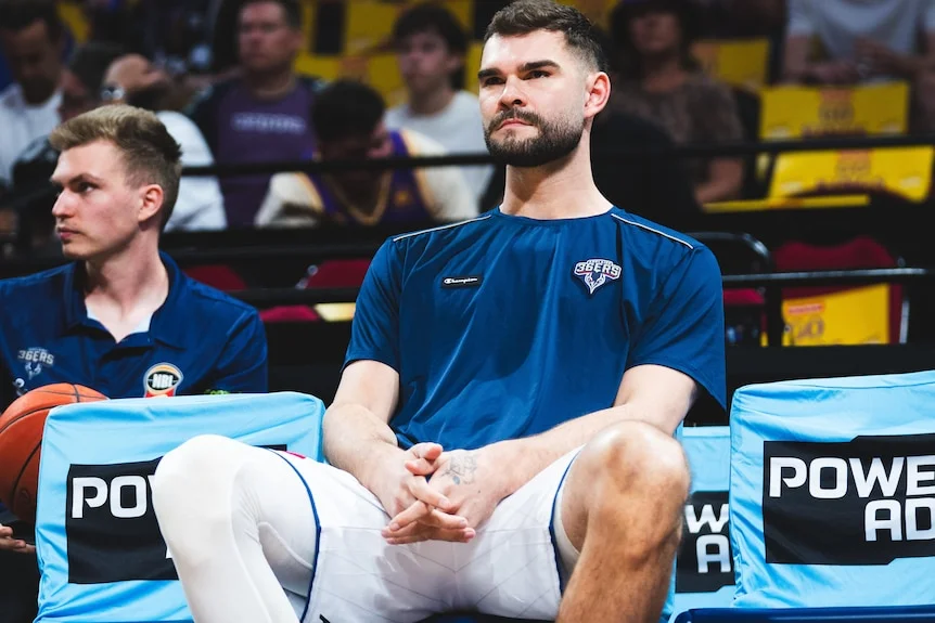 A man sits courtside while wearing compression socks over his right leg