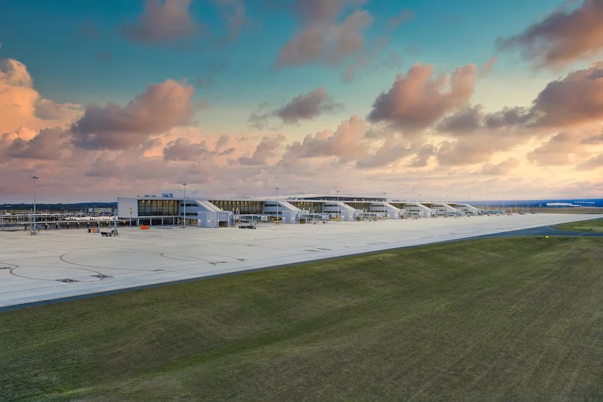 A wide shot of a brand new airport terminal from the outside and its runway on a sunrise morning.