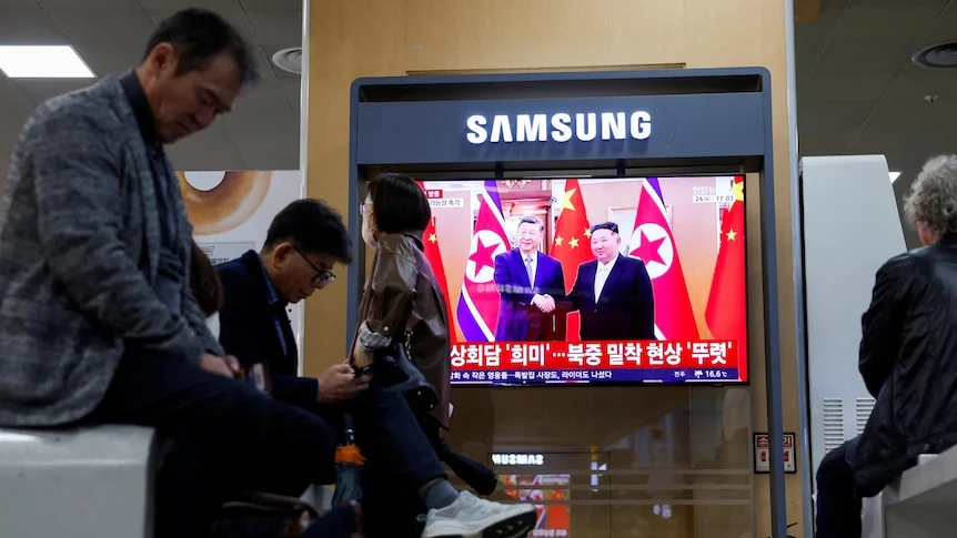 People watch a TV news report showing a handshake in front of Chinese and North Korean flags.
