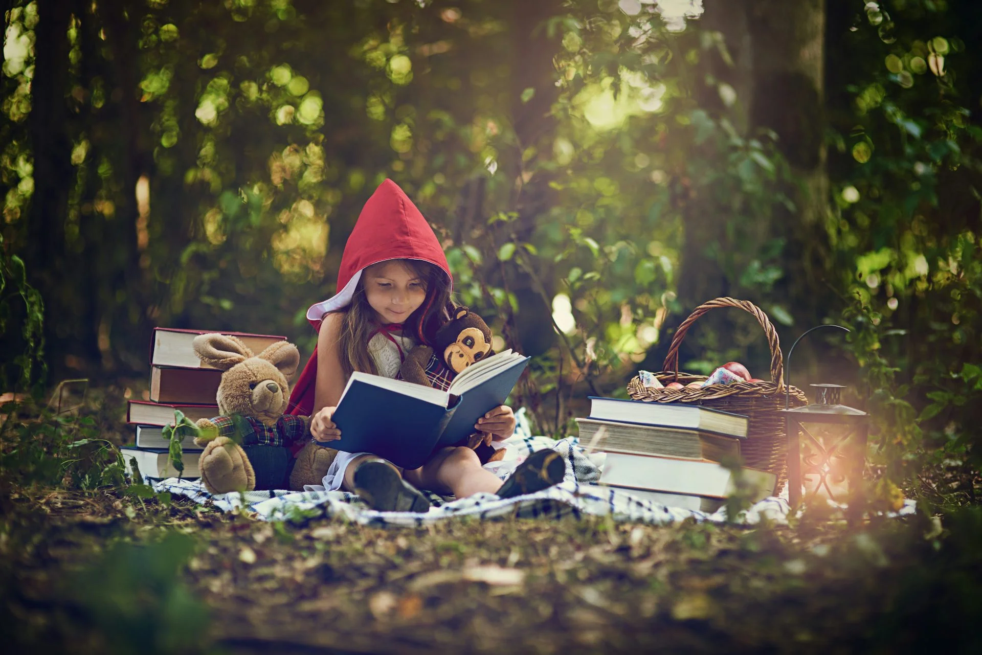 A young child wearing a red bonnet reads a book next to stuffed animals in a forest.