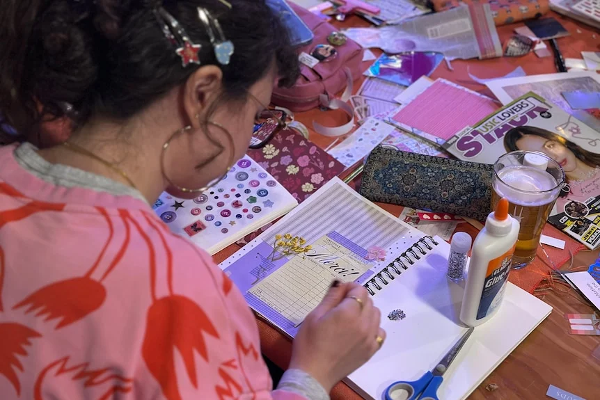 A woman decorating a scrapbook with craft supplies.