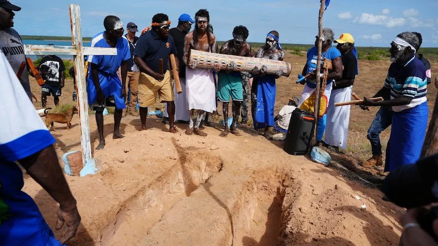 Men lay round painted logs containing the remains of their ancestors into bespoke graves.