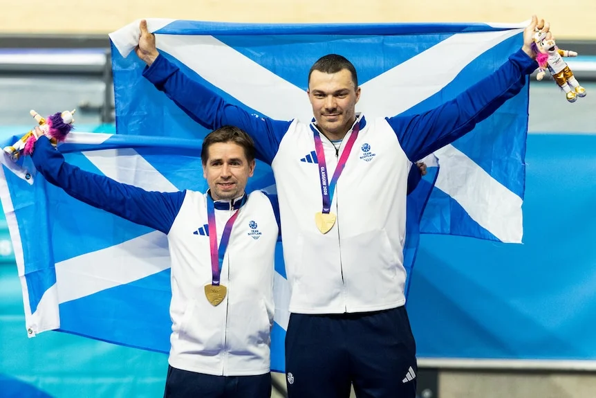 Neil Fachie and Aaron Pope hold Scotland flags on the cycling podium.