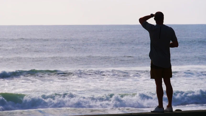 Man looks out over water with hand above head