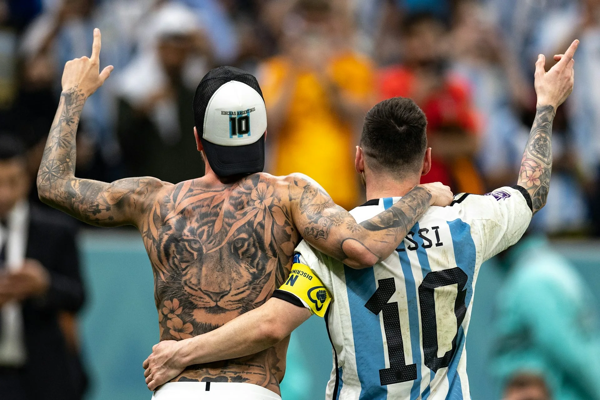A large tiger tattoo is visible on the bare back of one soccer player, while another player's arm tattoo can be seen as they raise their right hands after a victory.