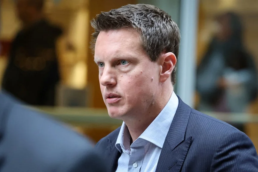 David Ellison, wearing a blue shirt and suit, leaves an office block.