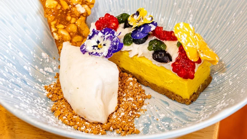 A yellow-coloured cheesecake covered in berries and plated up with ice cream.
