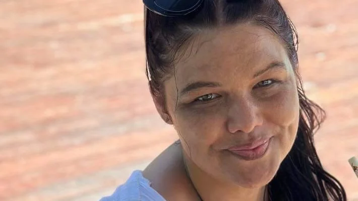 Woman with hazel eye and dark hair with sunglasses on head smiles at camera