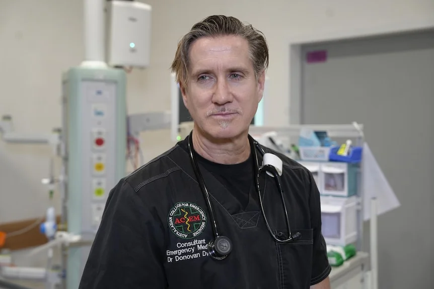 a man with blonde hair and goatee in scrubs with a stethoscope in hospital.