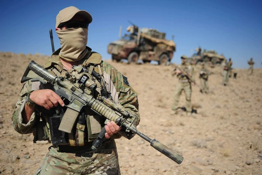 A soldier in the army sands before a dirt bank, hold a large gun.