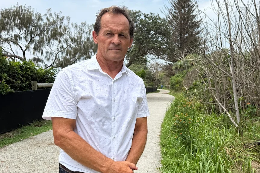 Man in while polo shirt on pathway beside dying trees.