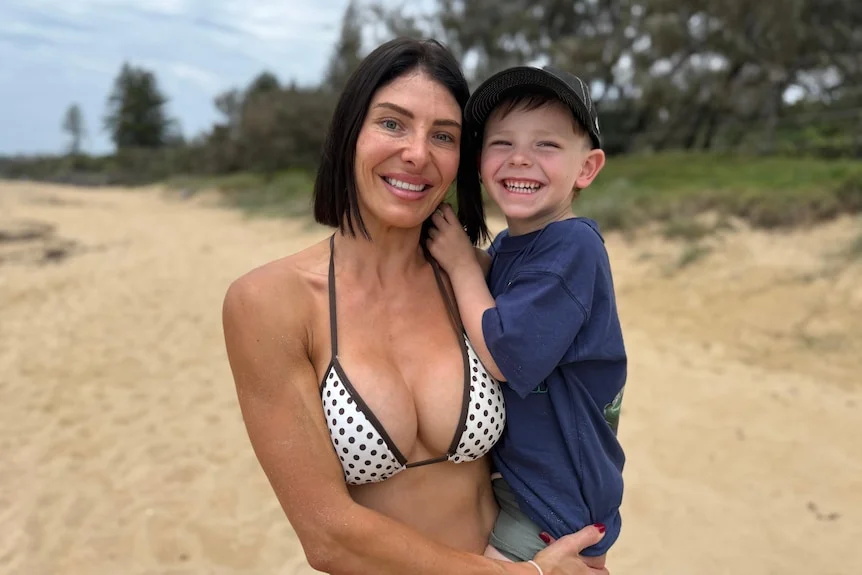 Woman in bikini smiling, holding young son in arms