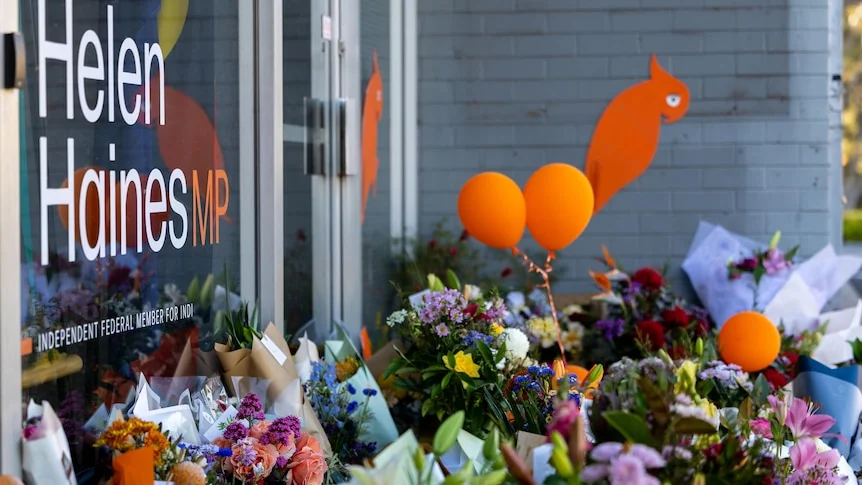 Flowers piled up outside an office with "Helen Haines MP" written on the facade.