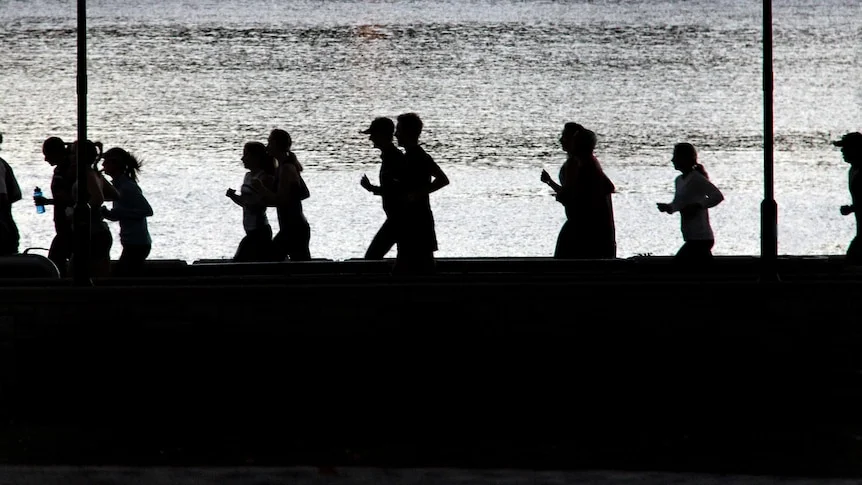 Silhouettes of people jogging along the river in the morning.