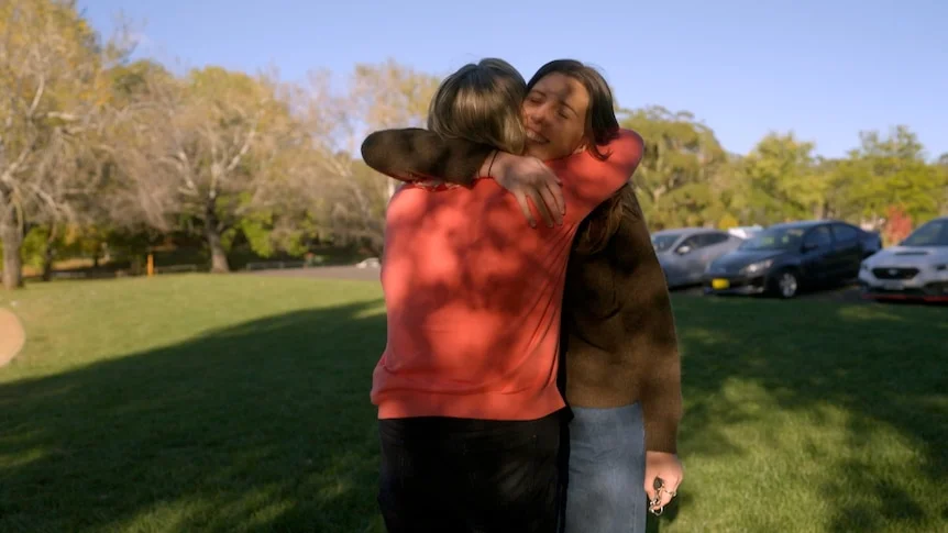 An older mother and late twenties daughter share a welcome home hug outdoors in Orange NSW.