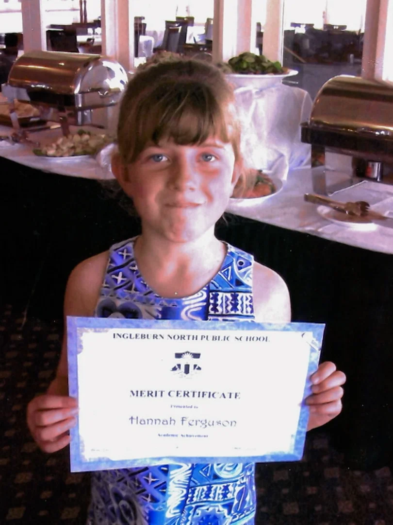 A female primary school student proudly holds up her school achievement award.
