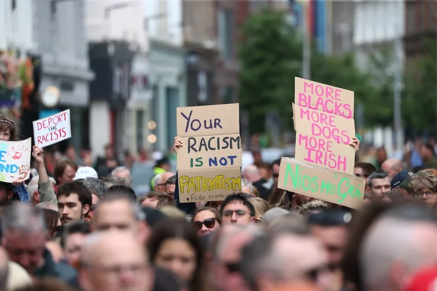 A large crowd holds up anti-racism signs in the middle of a city.