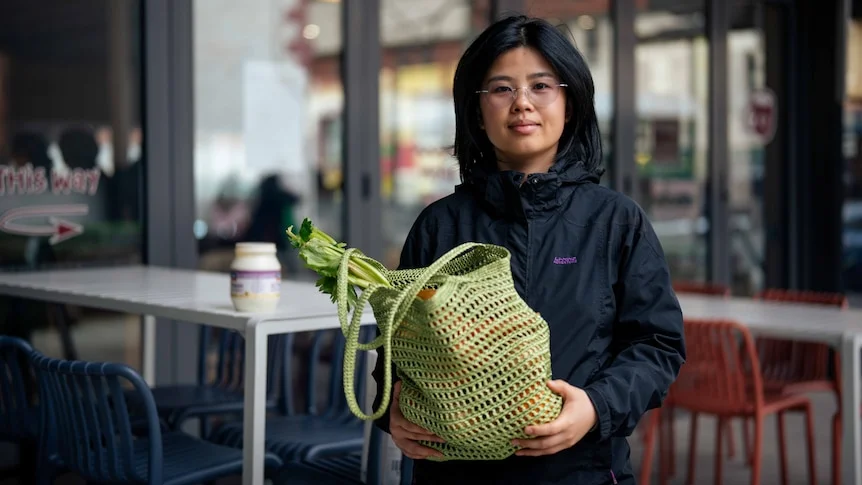 A woman smiles for a photo holding a grocery bag