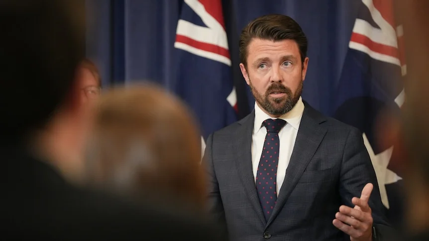 A man in a suit in front of two australian flags.