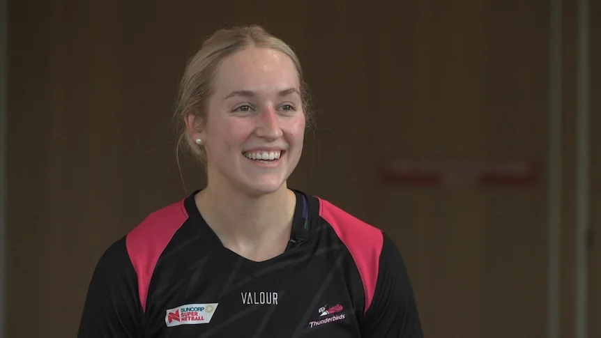 A smiling woman with blonde hair pulled back, wearing a black and pink top