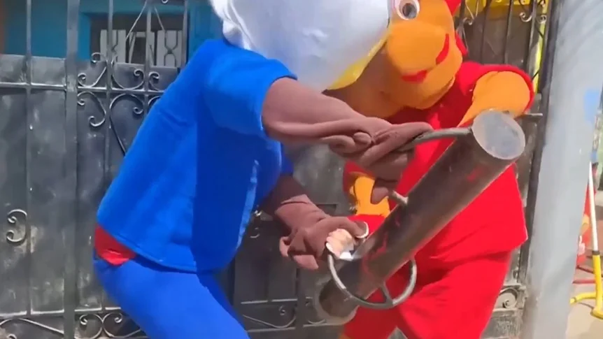 Two men in colourful costumes smash down a metal door.
