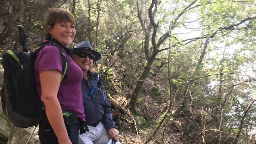 A woman and man in hiking gear surrounded by trees.