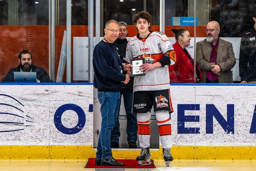 Dan Hogan on an ice rink speaking to a hockey player. 