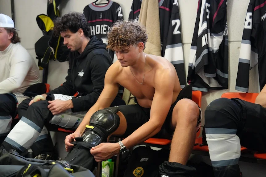Neil Pretorious inside a locker room putting his shin guards on. 