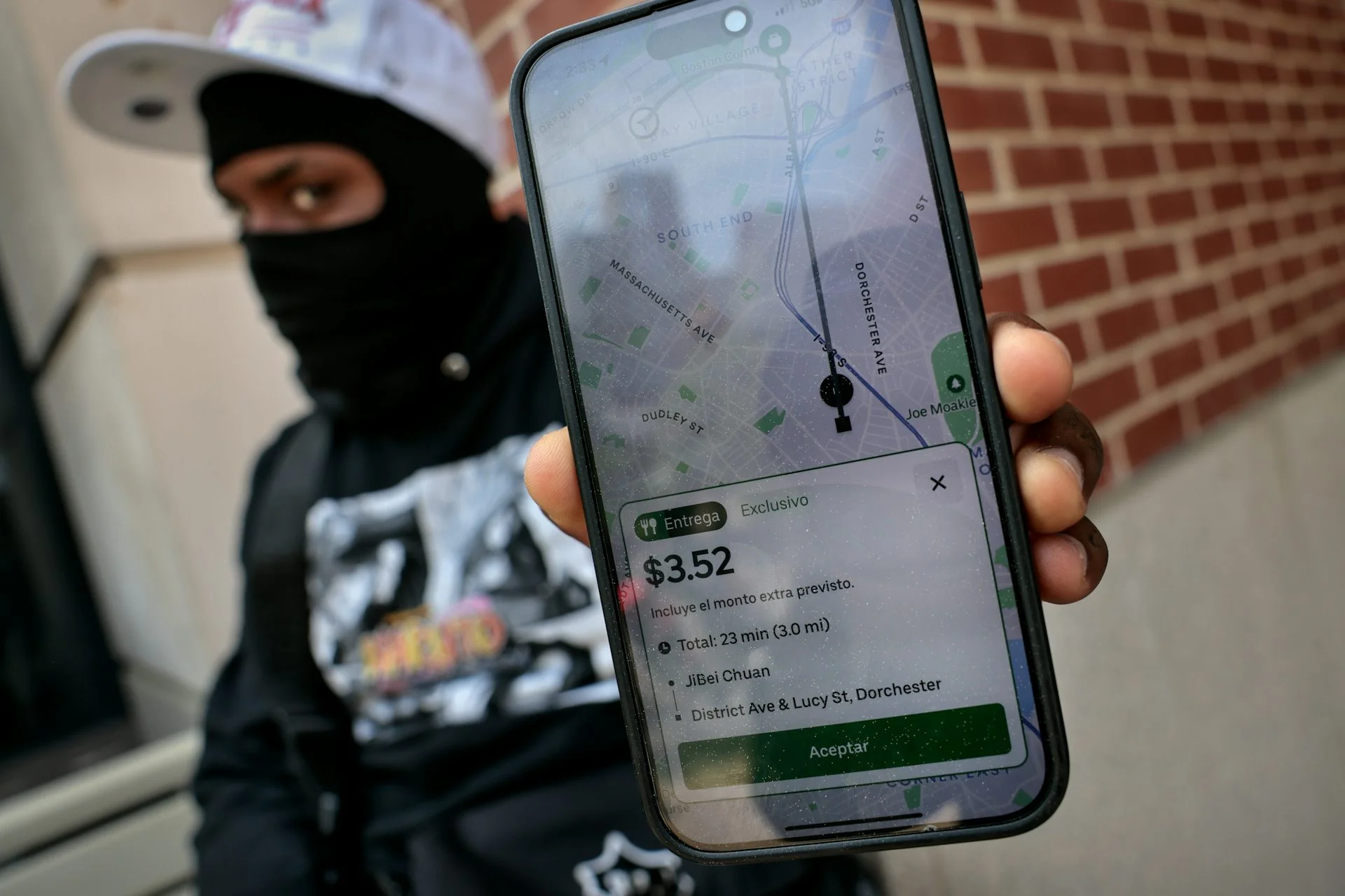 A food delivery gig worker holds up his smartphone with a food delivery order. The phone displays the information in Spanish.