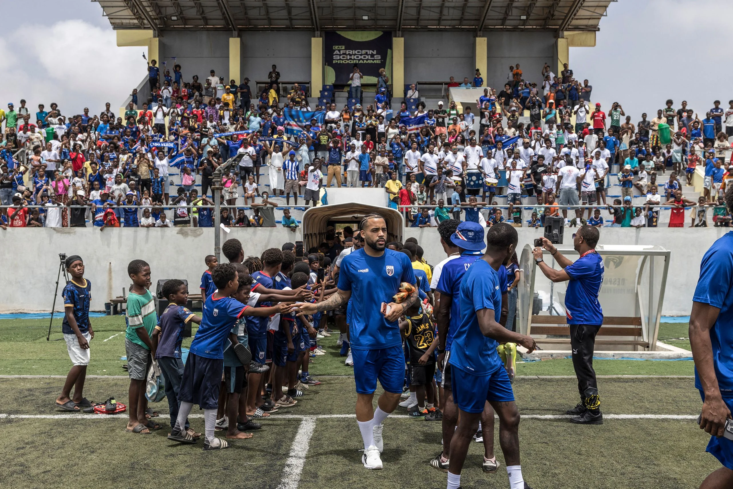 Soccer players walk down a line towards the camera behind them a crowd of people watches