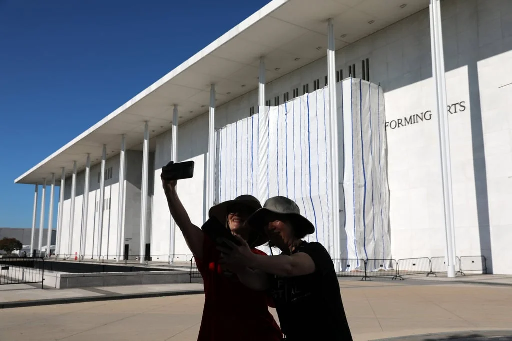 Women take selfies in front of the Kennedy Centre, where a tarp was set up for the removal of Trump’s name from the facade on Saturday. Photo: AP Women take selfies in front of the Kennedy Centre, where a tarp was set up for the removal of Trump’s name from the facade on Saturday. Photo: AP