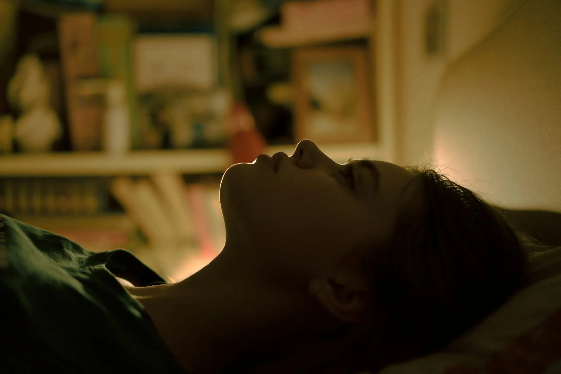 Teenage girl lying on her back in bed in near darkness with her eyes open.