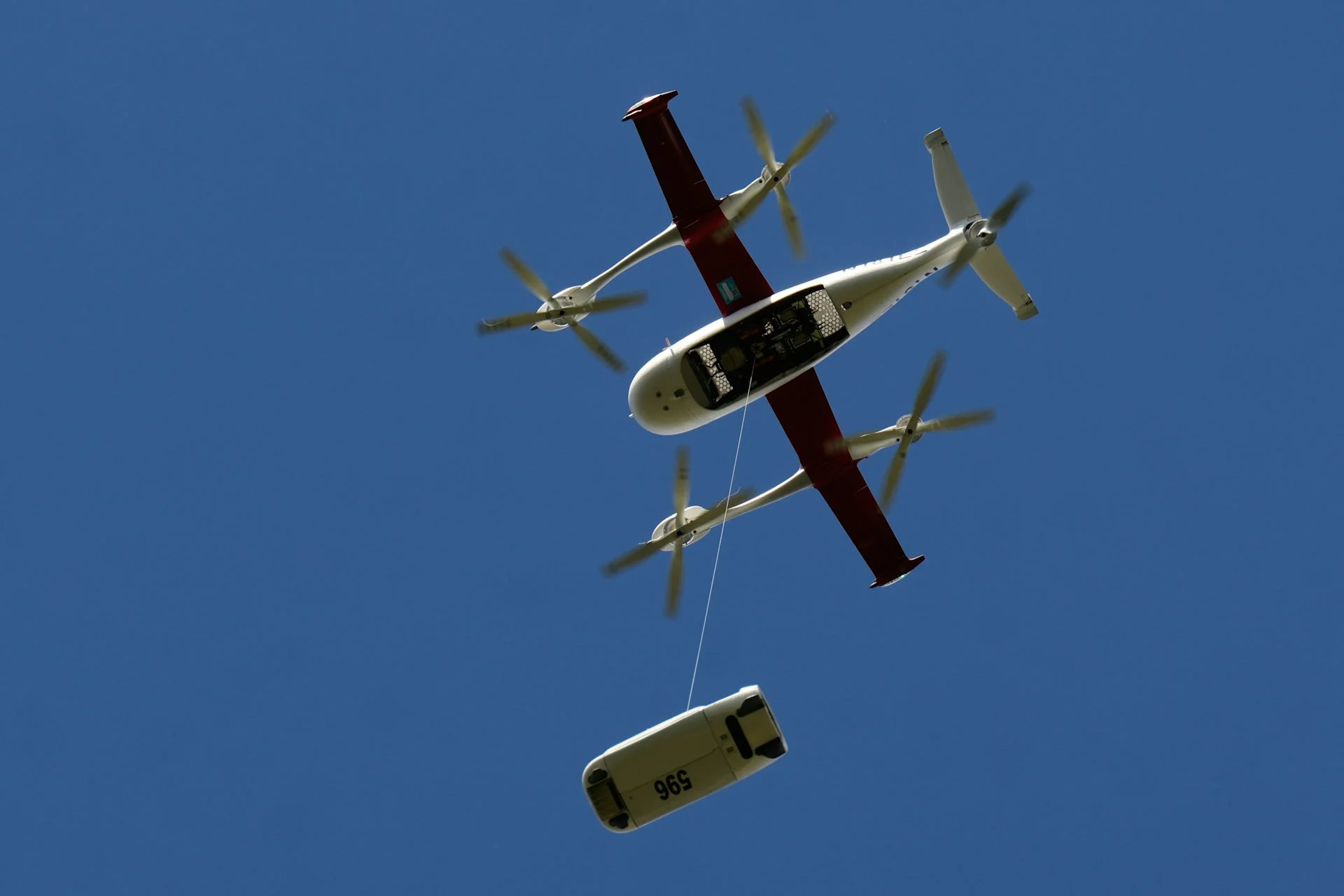 a small aircraft in the sky with an object suspended below it from a cable