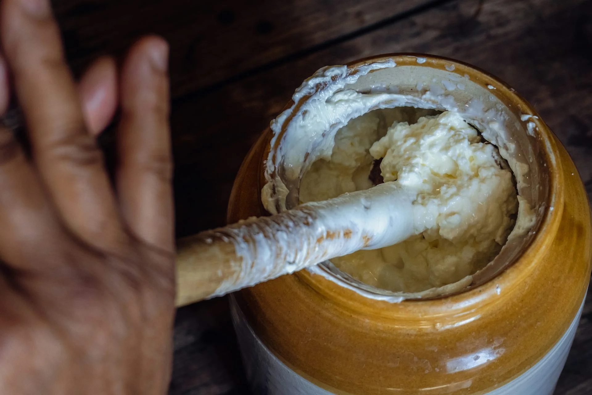 A person holding a long stick between the palms of their hands and using it to churn butter