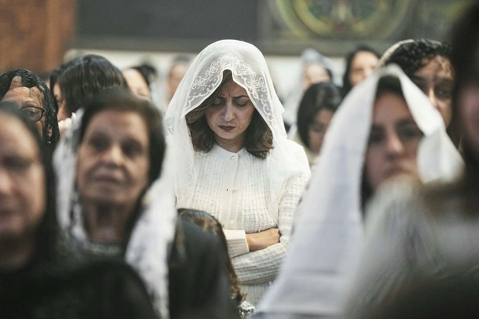 Women with white scarves draped over their heads stand in rows of pews.