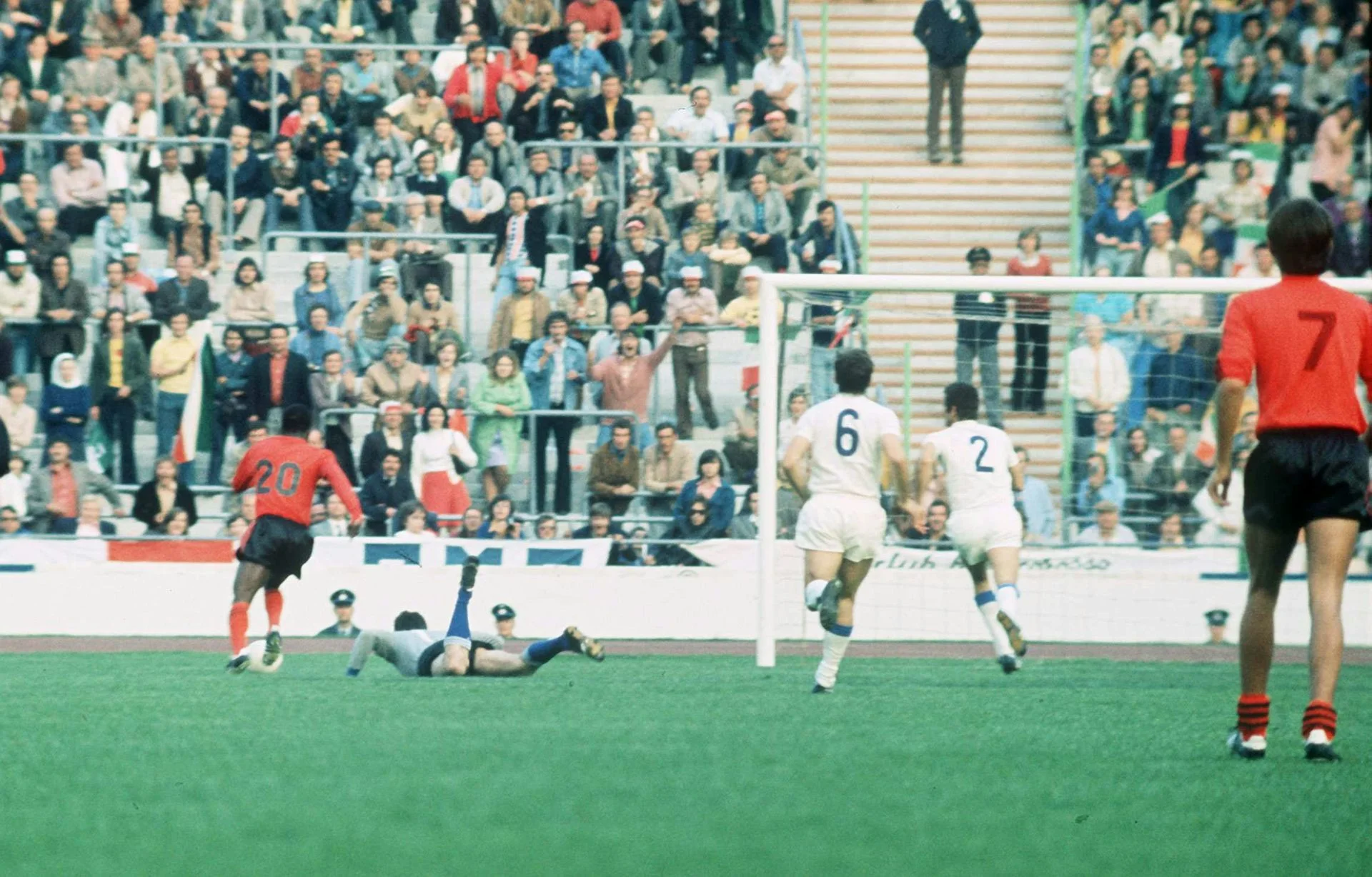 A group of men in white and orange jerseys stand on a football pitch.