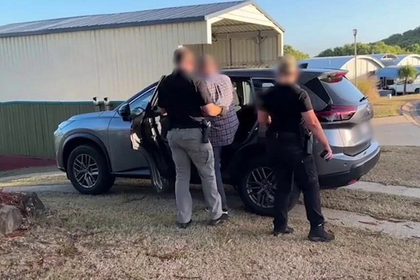 A man attempting to get into a car while police officer watch and handle him.