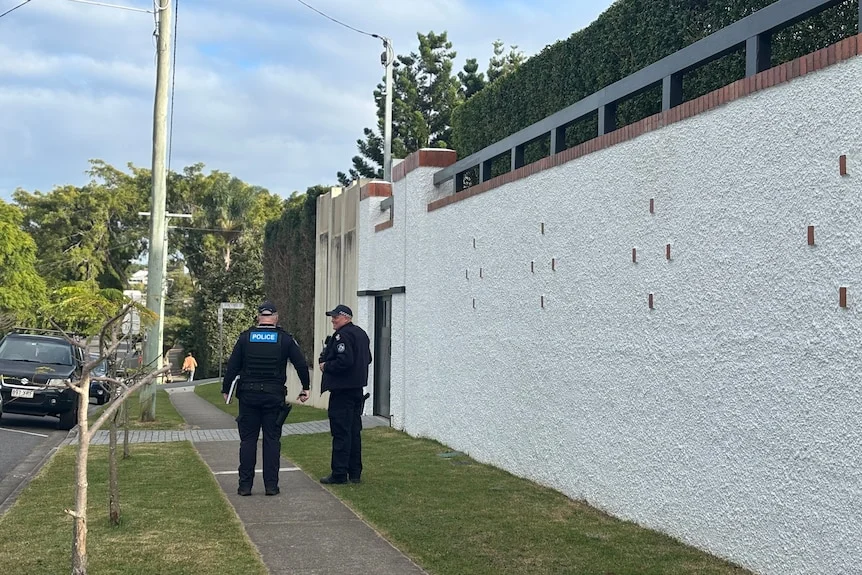 Police officers standing next to a white cement wall. 