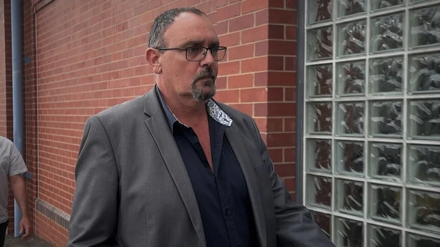 A middle-aged man with facial hair in a grey suit walks outside court.