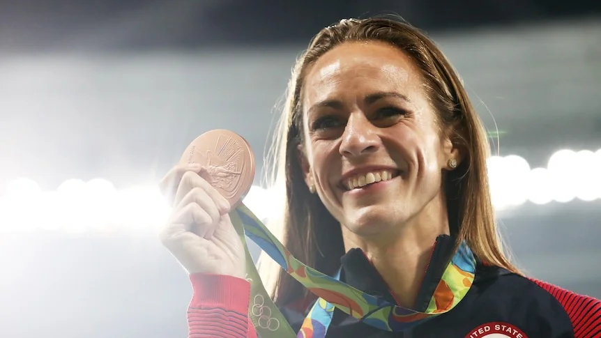 A woman holds a medal up to her face and smiles.
