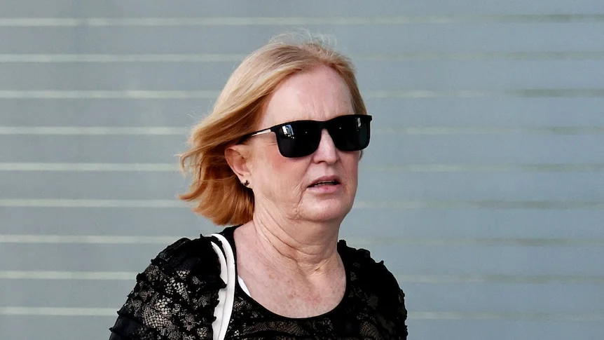A middle aged woman wearing dark sunglasses and a black tshirt.