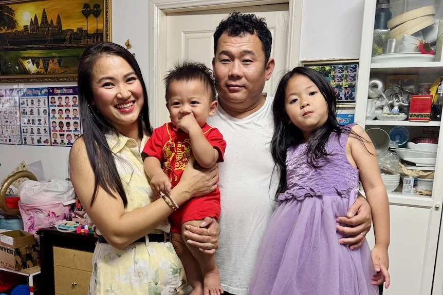A family of four, a mother to the left smiling with her baby boy, the father in the middle holding his daughter.