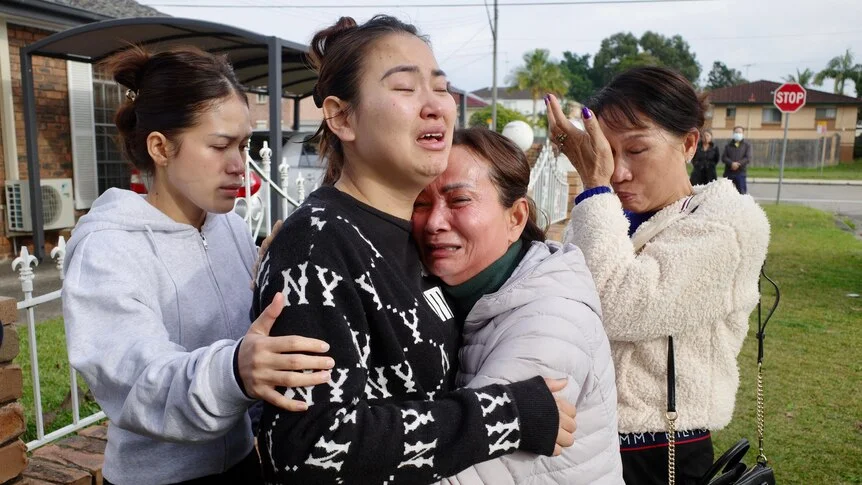 Woman in distress  wearing black and white jumper surrounded by teary women