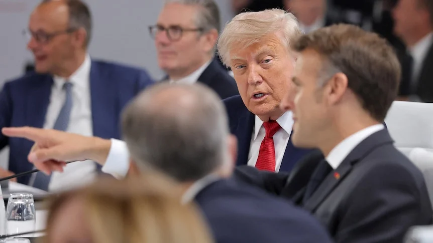 Donald Trump looks on as he is spoken to by emmanuel macron