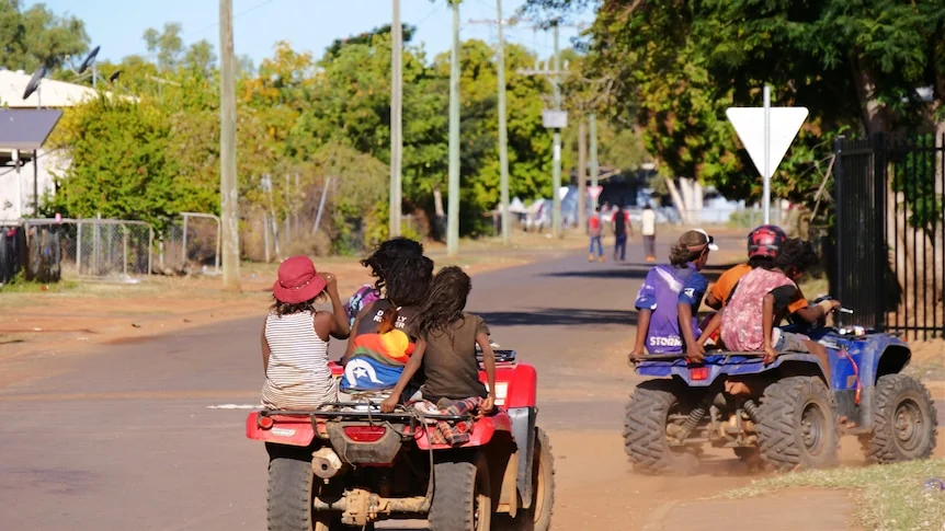 Children riding quad bikes on a rural street.