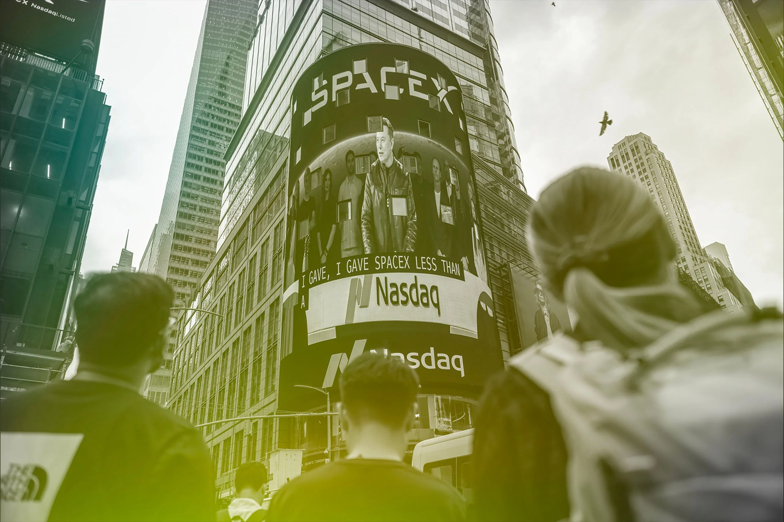 Figures look upwards towards a skyscraper where a billboard shows Elon Musk and reads Space X