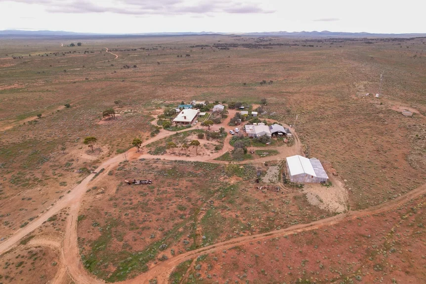 Farm buildings and a house in a brown landscape with low hills taken from a drone