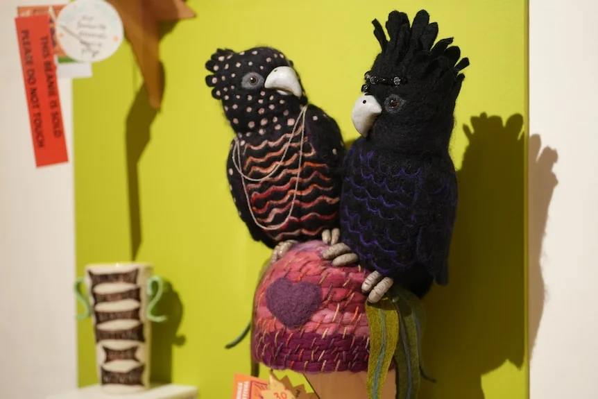 A pink felt knit beanie with two large black felted cockatoos on top of the beanie, looking at each other.